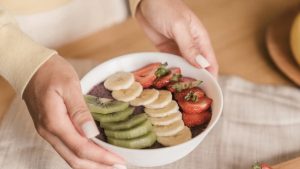 Delicious smoothie bowl topped with fresh fruits like kiwi, banana, and strawberries, held by manicured hands.